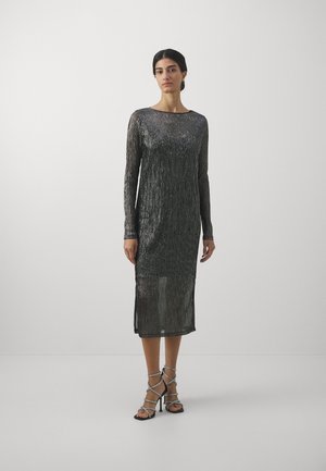Abito midi realizzato in tessuto nero scintillante con maniche lunghe, scollo a barca e spacchi laterali; abbinato a décolleté nere con stringhe.