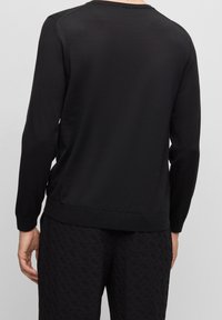 Schwarzer langärmeliger Pullover mit Rundhalsausschnitt, der eine glatte Textur, einen gerippten Saum und eine lockere Passform aufweist, kombiniert mit strukturierten schwarzen Hosen.