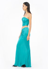 Teal crop top bez naramenica s naborima, u kombinaciji s dugom suknjom u istoj nijansi. Glatka tekstura, uski kroj i suptilno širenje na rubu.
