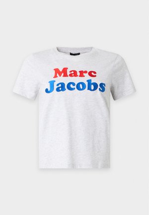 Jeune femme debout portant un t-shirt blanc Marc Jacobs, une jupe en jean avec des losanges en patchwork, des chaussettes blanches et des chaussures plates noires.