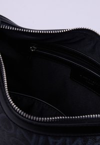 Interno nero di una borsa con chiusura a zip, caratterizzato da una trama di tessuto liscia e una tasca con zip aggiuntiva per l'organizzazione.