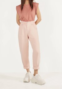 Ljusrosa löst sittande byxor med uppvikta ben och framfickor, i kombination med en kortärmad topp i dammig rosafärg och kraftiga vita sneakers.