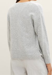 Pull en maille gris clair avec une coupe décontractée, ourlet et poignets côtelés, fentes latérales et tissu doux et texturé. Le design comprend un col ras du cou.