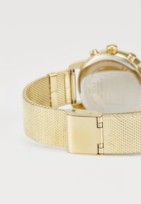Goldenes Mesh-Uhrenarmband mit einem gebürsteten Metallverschluss. Das Uhrengehäuse hat eine glatte Oberfläche und dezente Details auf der Rückseite.