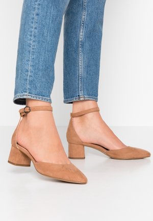 Schoenen met hoge hak van beige suède, met een spitse neus, hoekige vorm en een blokhak van gemiddelde hoogte. Voorzien van een enkelriempje met een ronde gesp als detail.