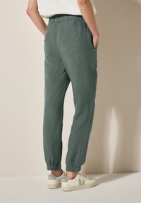 Lätta, avsmalnande joggers i mörkgrön tyg med elastisk midja och muddar, som har två bakfickor och en texturerad yta.