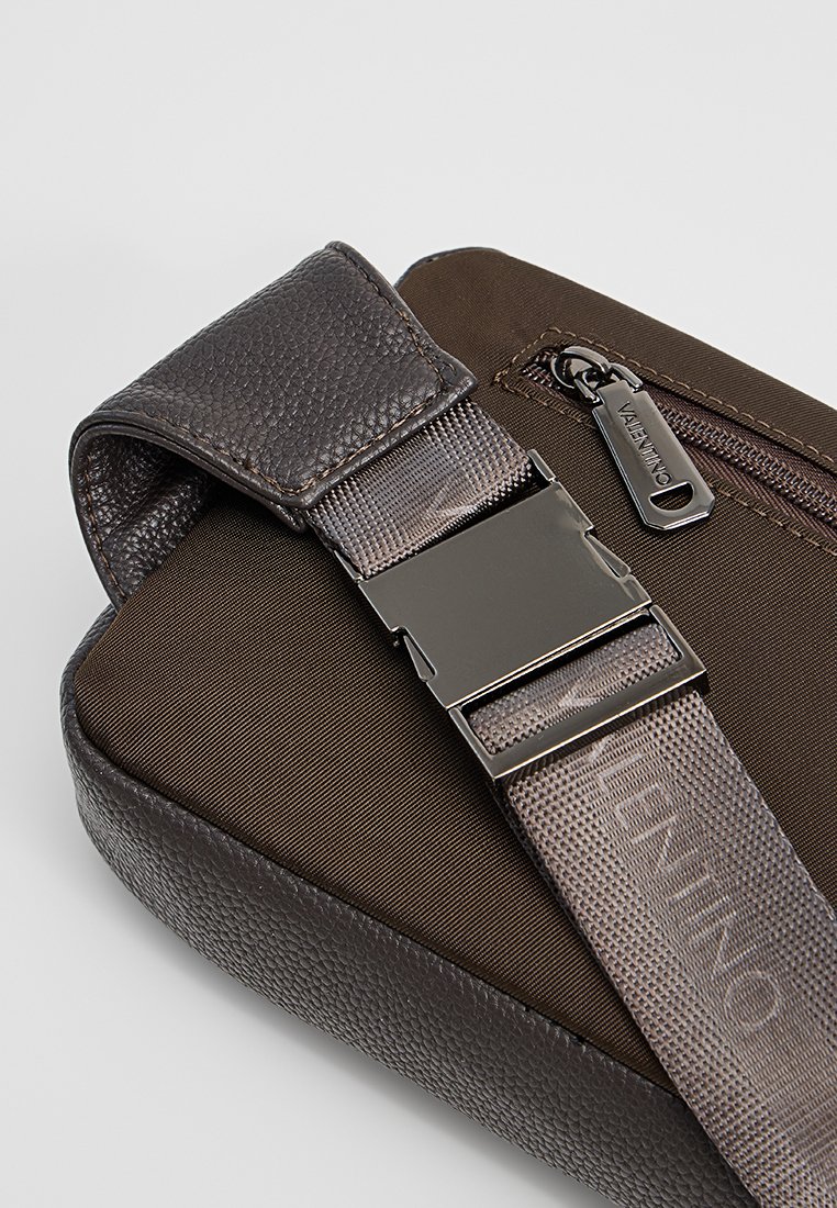 Bolso de cuero texturizado marrón con forma rectangular, que presenta una correa gris, herrajes plateados y un bolsillo con cremallera.