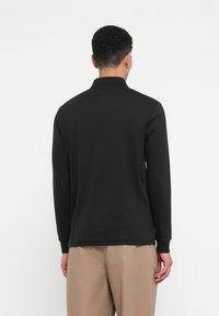 Polo shirt a maniche lunghe nera in cotone, con colletto classico e taglio dritto. Design semplice senza loghi o motivi visibili.