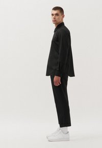 Camisetta nera a maniche lunghe con colletto, abbinata a pantaloni neri su misura e sneakers bianche; texture morbida, design semplice e linee pulite.