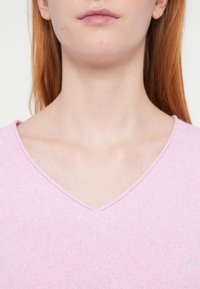 Ροζ πλεκτό πουλόβερ με V-λαιμόκοψη και ριμπ ύφανση, με διακριτικές διακυμάνσεις στο χρώμα και εφαρμοστή γραμμή.