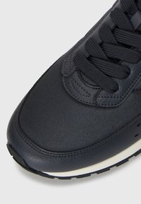 Navy leather sneaker with textured surface, rounded toe, and black laces. Notable white midsole and contrasting stitching.
