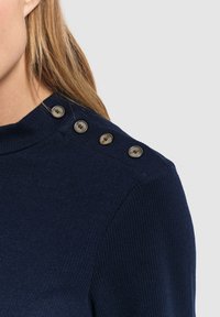 Granatowy sweter z prążkowanym wzorem, z okrągłym dekoltem i czterema dużymi, okrągłymi guzikami na jednym ramieniu. Materiał wydaje się miękki i strukturalny.