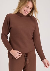 Bruine gebreide trui met een nepkraag, geribbelde manchetten en een losse pasvorm. Gladde textuur, gecombineerd met bijpassende broek met trekkoord.