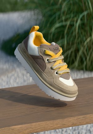 Beige en bruine suède sneaker met witte mesh accenten, gele veters en een witte rubberen zool. Beschikt over een gestructureerd bovenwerk en een logo op de tong.