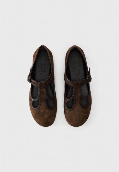 Brown suede Mary Jane shoes featuring cut-out detailing, a strap with a buckle, and a smooth leather inner lining. Flat soles.