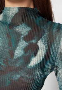 Pleated textile top featuring an abstract teal and dark gray pattern, high neckline, and ribbed texture.