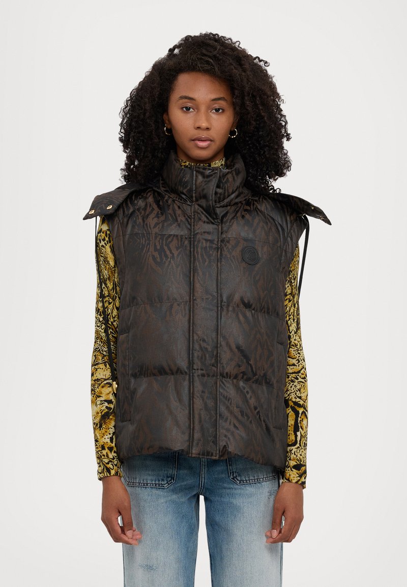 Gilet imbottito marrone con finitura lucida, colletto alto e dettagli con bottoni a pressione. Presenta un logo impresso e si abbina a una camicia a fantasie.