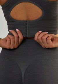 Szara sportowa biustonosz z wycięciem na plecach, z zapięciem na haczyk, prążkowaną teksturą i współgrającymi legginsami z wysokim stanem o bezszwowym wzorze.