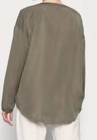 Blusa verde oliva a maniche lunghe realizzata in un tessuto morbido e leggero. Presenta un orlo arrotondato e spalle leggermente scese.