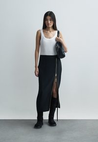 Czarna spódnica na suwak z przodu z bocznymi rozporkami, zestawiona z białym topem na ramiączkach. Stylizację dopełniają czarne botki i mała czarna torebka. Gładka faktura tkaniny.