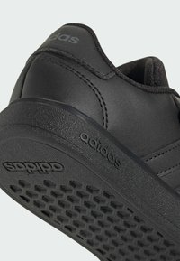 Czarny syntetyczny sneaker z teksturowaną podeszwą, z trzema bocznymi paskami i wytłoczonym logo na pięcie. Gładka powierzchnia górna.