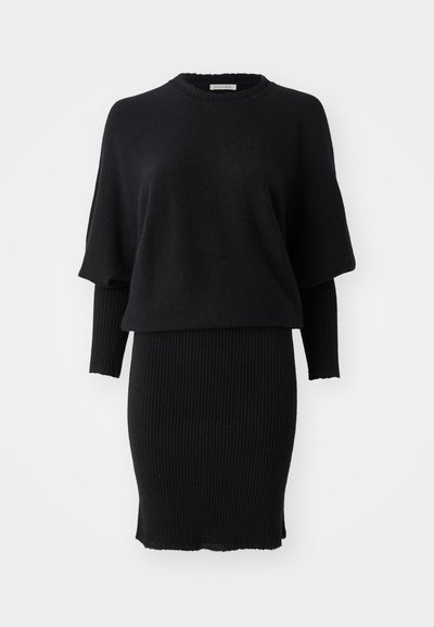 Abito in maglia nera con gonna a tubo a righe e top a maniche corte oversize sovrapposto a una camicia attillata a maniche lunghe, colletto rotondo.