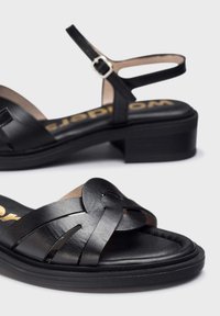 Sandales en cuir noir avec un design tissé sur le dessus, une sangle à la cheville, un talon bas et une semelle rembourrée. Accentué par un logo doré.