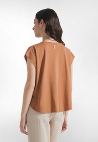 Kortærmet, afslappet pasform top i brændt orange bomuld. Har rund hals og et lille mærke på ryggen. Glat tekstur med en let buet kant.