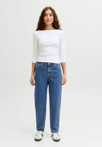 Balta garām piedurknēm krekls, zilas taisnas bikses, melnas un baltas sporta kurpes. Vienkāršs dizains ar brīvu piegriezumu un mīkstu tekstūru.