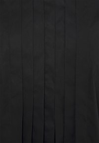 Tissu noir avec des plis verticaux, texture lisse et lignes épurées. Le matériau semble léger et structuré. Aucun élément métallique ou accent visible.