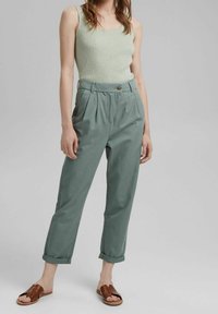 Light green ribbed tank top paired with high-waisted, tapered olive green pants featuring a button closure and rolled cuffs. Brown slider sandals.