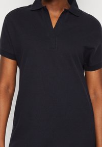 Camisa polo azul marino con cuello clásico, mangas cortas y un acabado de tela texturizada, que presenta una tapeta limpia y sutiles detalles de costura.