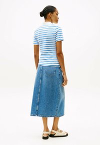 Stribet blå og hvid kortærmet skjorte, parret med en lang denim-nederdel. Sandalerne har lyse stropper og en flad sort sål.