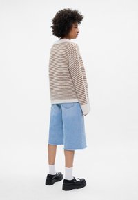 Raidallinen neule vaaleanbeigellä ja kermansävyllä, yhdistettynä vaaleansinisiin farkkushortseihin. Mustat korokepohjaiset kengät ja valkoiset sukat täydentävät asun.