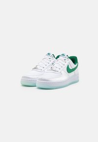 White leather sneakers with green accents, featuring a smooth texture, rounded toe, and translucent light blue sole. Silver detailing on laces.