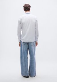 Vaaleansininen pitkähihainen paita ja leveälahkeiset siniset farkut. Paidassa on suora leikkaus ja napilliset kalvosimet; farkuissa on korkeavyötärö ja takataskut.