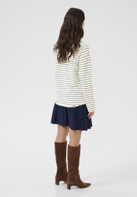 Maglia a maniche lunghe a righe cremisi e navy, abbinata a una gonna plissettata navy e stivali alti fino al ginocchio in camoscio marrone, vista da dietro.