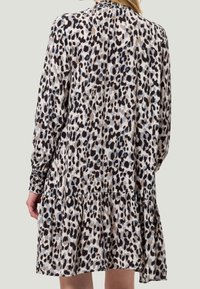 Femme portant une robe à manches longues, ample, avec des poignets smockés et un motif léopard noir, marron et gris.