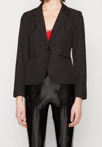 Svart skräddarsydd blazer med spetsslag, enkel knappstängning, två framfickor och något strukturerade axlar. Slät tygfinish.