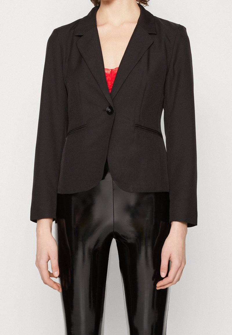 Svart skräddarsydd blazer med spetsslag, enkel knappstängning, två framfickor och något strukturerade axlar. Slät tygfinish.