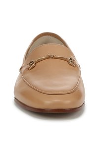 Tan leren instappers met een ronde neus, een gladde textuur, gestikte accenten en een gouden hardware detail aan de voorkant. Platte, bruine zool.