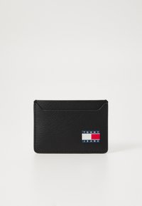 Crni kožni novčanik za kartice s teksturiranom površinom, dvije utora za kartice i dekorativnim logotipom u crvenoj, bijeloj i plavoj boji.