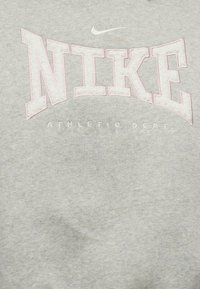 Γκρι ύφασμα με μεγάλο λευκό και ροζ περίγραμμα του κειμένου "NIKE" και μικρότερο λευκό κείμενο "ATHLETIC DEPT." από κάτω, με λευκό σήμα Nike από πάνω.