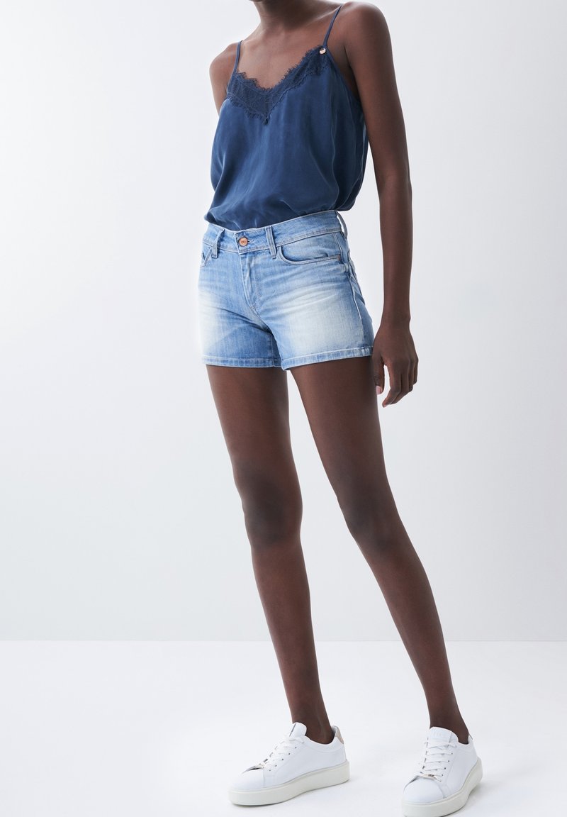 Shorts en denim bleu clair avec un effet délavé, comprenant cinq poches et une fermeture éclair classique. Associés à un caraco bleu marine.