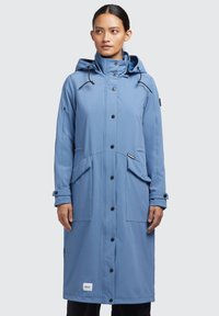 Abrigo largo impermeable en azul claro con capucha, que presenta botones negros, un bolsillo con cremallera y dos bolsillos frontales para almacenamiento. Textura de tejido suave.
