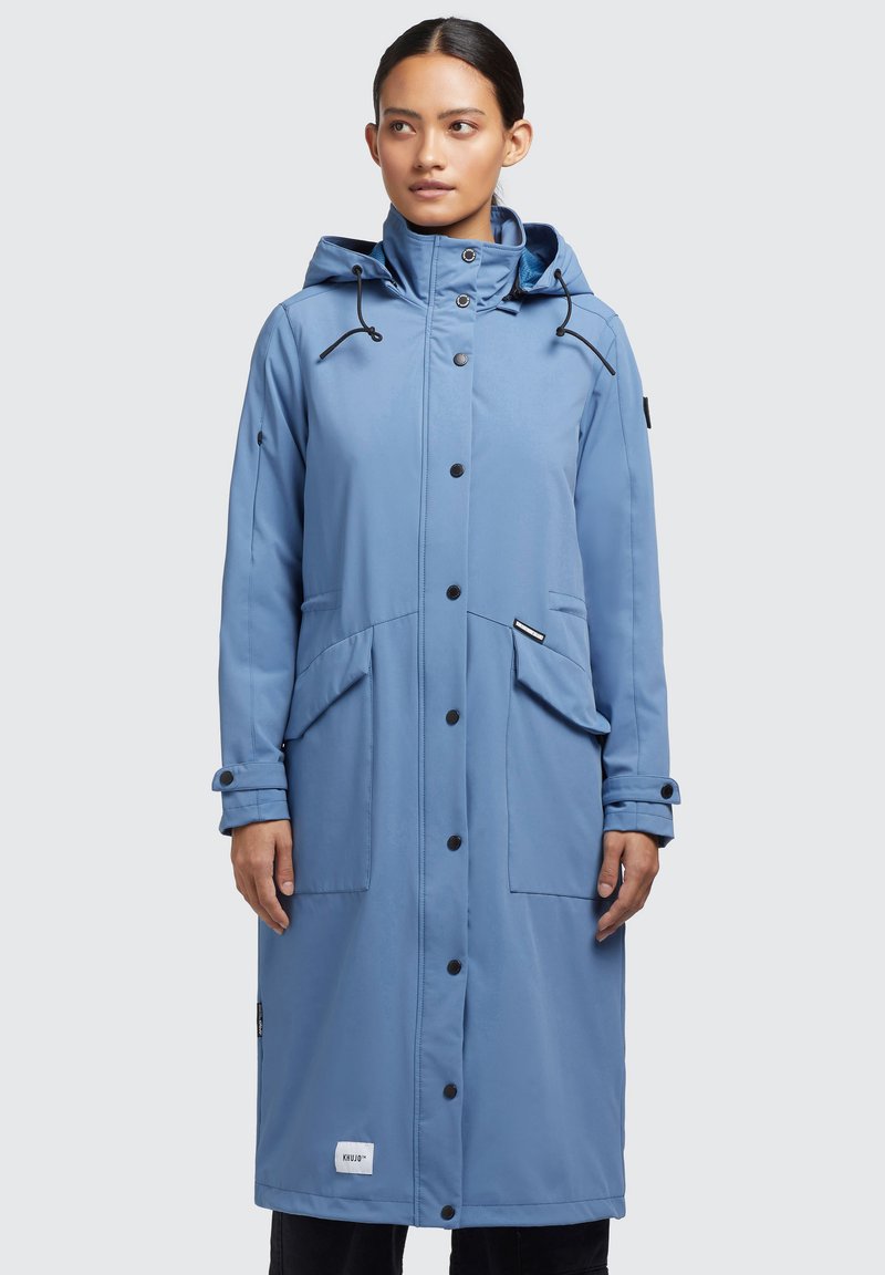 Abrigo largo impermeable en azul claro con capucha, que presenta botones negros, un bolsillo con cremallera y dos bolsillos frontales para almacenamiento. Textura de tejido suave.