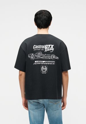 Osoba ubrana w czarny t-shirt z białym napisem "Castrol GTX Racing" i grafiką samochodu wyścigowego na plecach, w połączeniu z jasnoniebieskimi dżinsami.