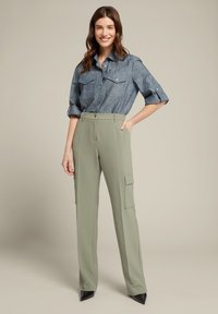 Blauwe chambray blouse met opgerolde mouwen, gecombineerd met hooggetailleerde olijfgroene cargobroek met zakken en zwarte spitse hakken.
