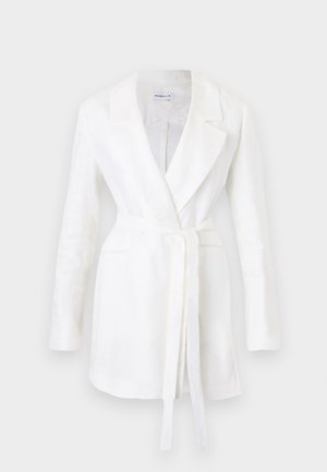 Blazer blanc à manches longues avec revers crantés, deux poches avant et une ceinture à nouer à la taille, suspendu sur un fond uni.