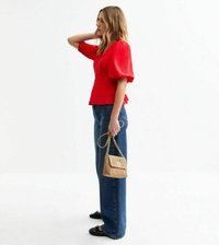 Haut rouge texturé avec des manches ballon, associé à un jean bleu taille haute. Comprend également un petit sac à main en osier doré et des chaussures plates noires.